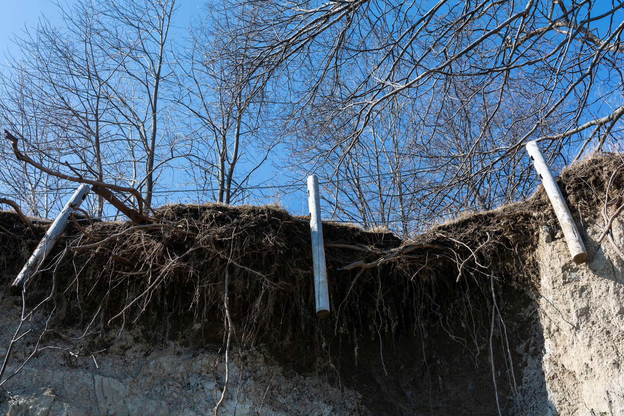 Fence posts hang by cables after the soil holding them has been eroded 