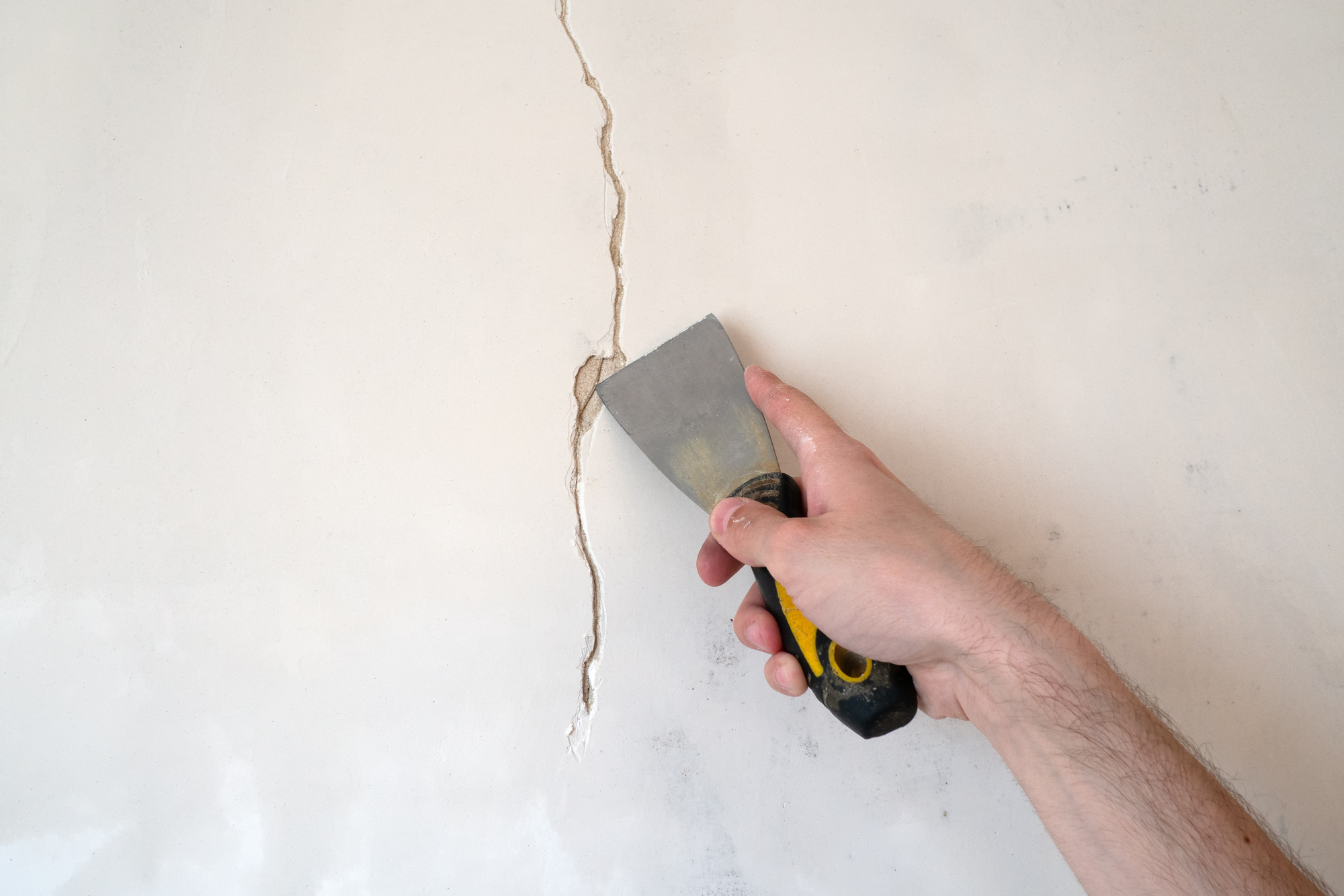 Construction man worker repairing a crack wall of a home, plastering cement on wall. Builder applying white cement to a crack in a wall with a putty knife. close up